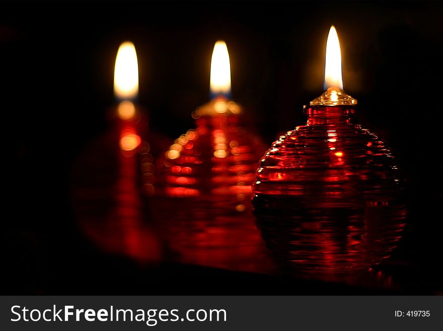 Three red oil lamps standing on a shelf. Focus is on the one in front.