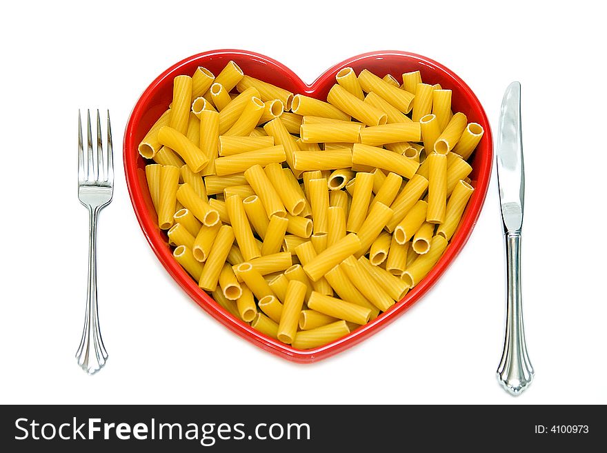 A red heart dish filled with rigatoni pasta - knife, fork on white background. A red heart dish filled with rigatoni pasta - knife, fork on white background.