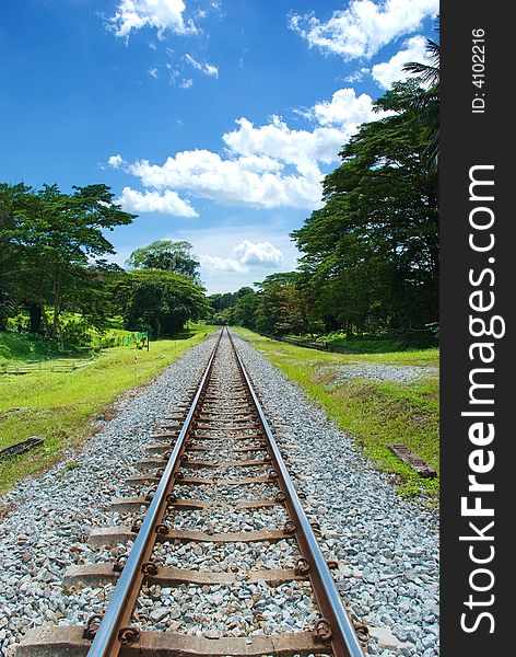 Straight railway track converging in the distance under a partly cloudy blue bright sky. Straight railway track converging in the distance under a partly cloudy blue bright sky