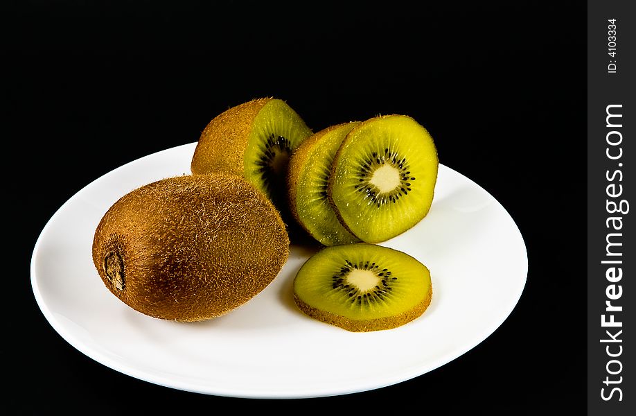 Sliced kiwi fruits on a white plate, black background. Sliced kiwi fruits on a white plate, black background