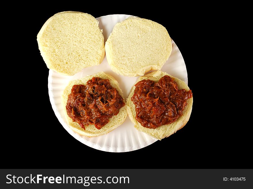 Two barbecue beef sandwiches on a paper plate against a black background. Two barbecue beef sandwiches on a paper plate against a black background.