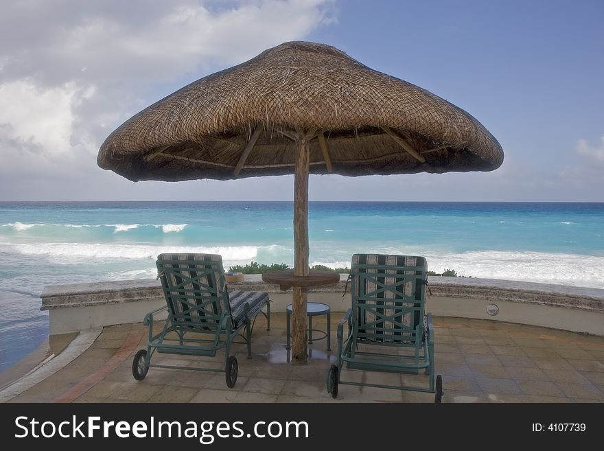 Two chairs and a table under a straw umbrella looking to sea. Two chairs and a table under a straw umbrella looking to sea