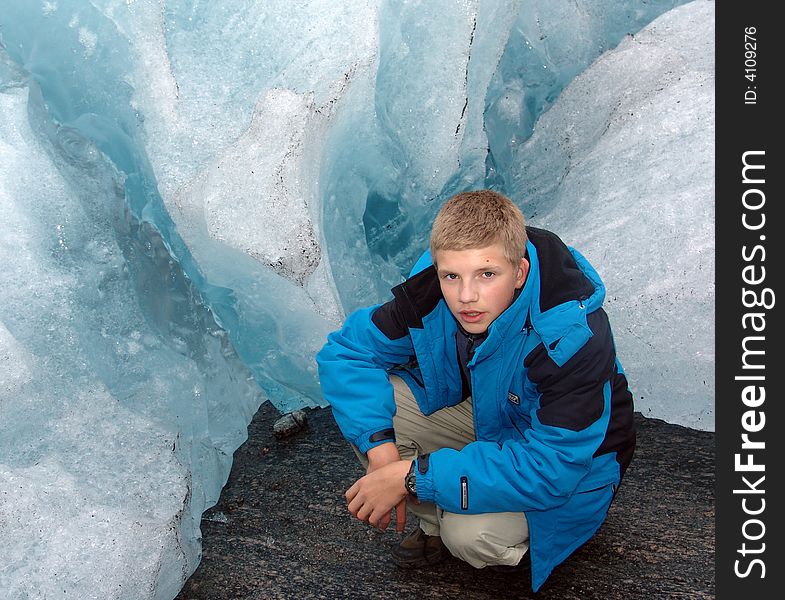 The teenager sits at edge(territory) of the glacier which is climbing down a mountain