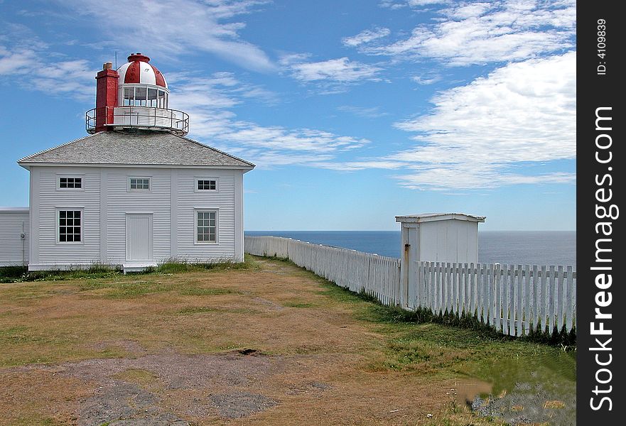 New Foundland CA lighthouse with ocean and blue sky in background. White structure with red and white domed top and white picket fence running along the top of the cliff overlooking ocean. New Foundland CA lighthouse with ocean and blue sky in background. White structure with red and white domed top and white picket fence running along the top of the cliff overlooking ocean.