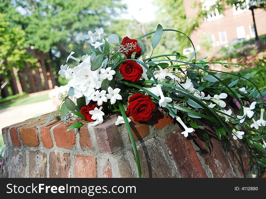 Beautiful bride's bouquet lying on a brick column.  Red roses along with other white flowers and greenery adorn this arrangement.