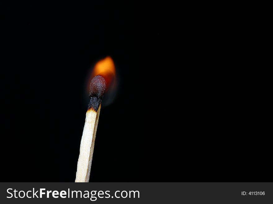 Close of a matchstick lit against a dark background. Close of a matchstick lit against a dark background