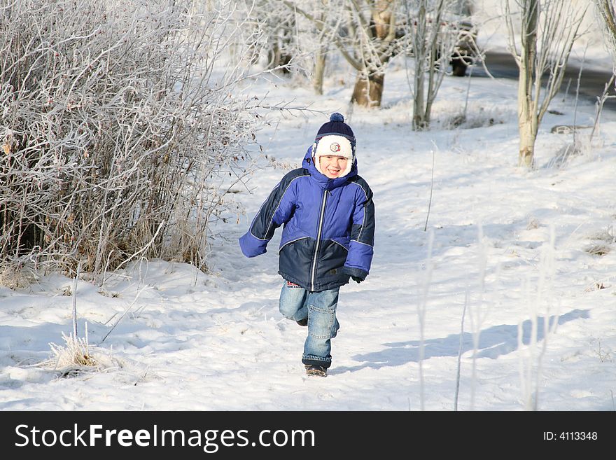The boy runs in the winter on a footpath in park. The boy runs in the winter on a footpath in park