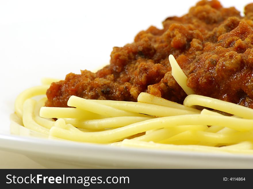 Fresh cooked white spaghetti pasta and juicy tomato meat sauce, often referred to as Italian Spaghetti, on white porcelain plate and white background. Close up macro and unique side perspective. Fresh cooked white spaghetti pasta and juicy tomato meat sauce, often referred to as Italian Spaghetti, on white porcelain plate and white background. Close up macro and unique side perspective.