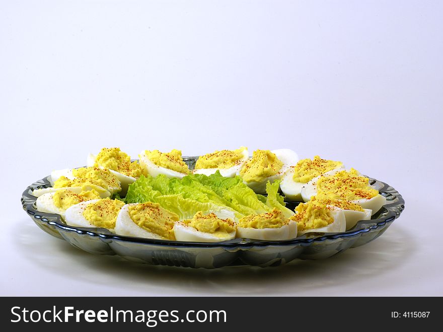 Homemade deviled eggs with a dash of cayenne pepper, displayed on depression era blue glass platter over white background. Small touch of baby lettuce completes the arrangement.