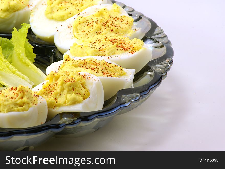 Homemade deviled eggs with a dash of cayenne pepper, displayed on depression era blue glass platter over white background. Small touch of baby lettuce completes the arrangement.