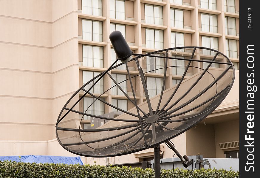 A satellite communication dish of black mesh in front of a hotel. A satellite communication dish of black mesh in front of a hotel