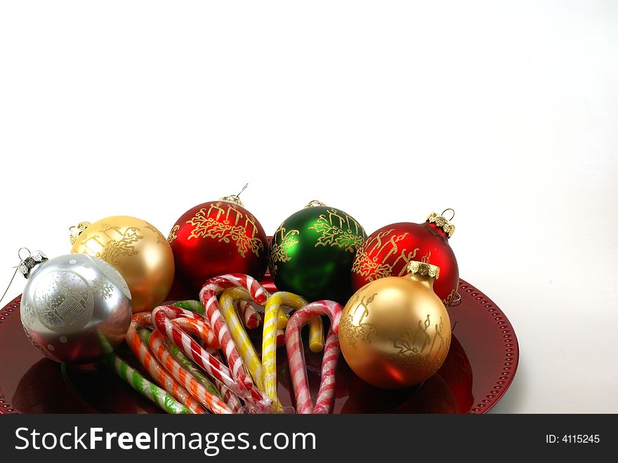 Shiny Christmas ornaments on red platter with wrapped candy canes in the middle. White background with copy space. Shiny Christmas ornaments on red platter with wrapped candy canes in the middle. White background with copy space.