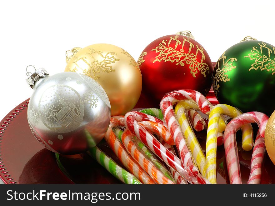 Shiny Christmas ornaments on red platter with wrapped candy canes in the middle. White background with copy space. Shiny Christmas ornaments on red platter with wrapped candy canes in the middle. White background with copy space.