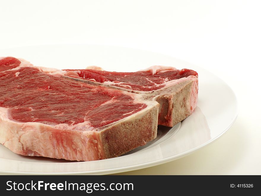 Very large and thick, fresh, juicy uncooked tbone steak on white plate with copy space. Very large and thick, fresh, juicy uncooked tbone steak on white plate with copy space.