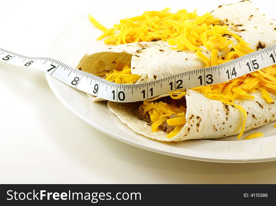 Homemade beef and bean mexican/spanish burritos wrapped in grilled white tortillas with shredded cheddar cheese. Measuring tape draped across for fitness and weight loss concepts. Homemade beef and bean mexican/spanish burritos wrapped in grilled white tortillas with shredded cheddar cheese. Measuring tape draped across for fitness and weight loss concepts.