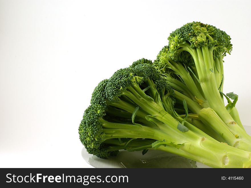 Large bunch of raw broccoli with leaves and stems on white plate.