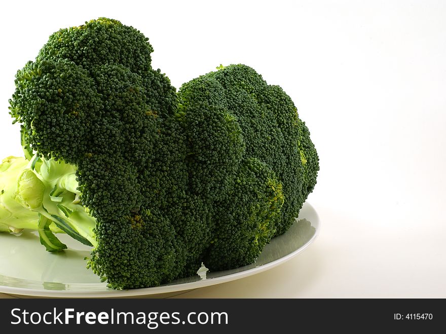 Large bunch of raw broccoli with leaves and stems on white plate.