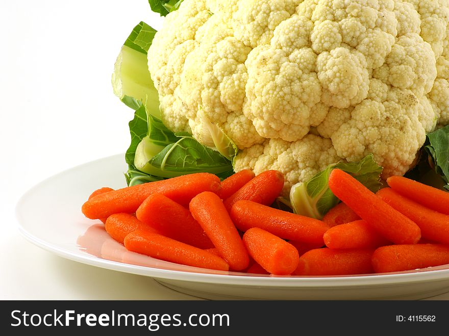 Raw cauliflower and baby carrots on white plate with greenery. Raw cauliflower and baby carrots on white plate with greenery.