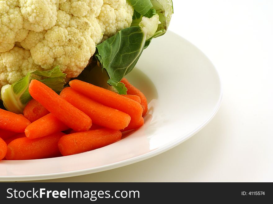 Raw cauliflower and baby carrots on white plate with greenery. Raw cauliflower and baby carrots on white plate with greenery.