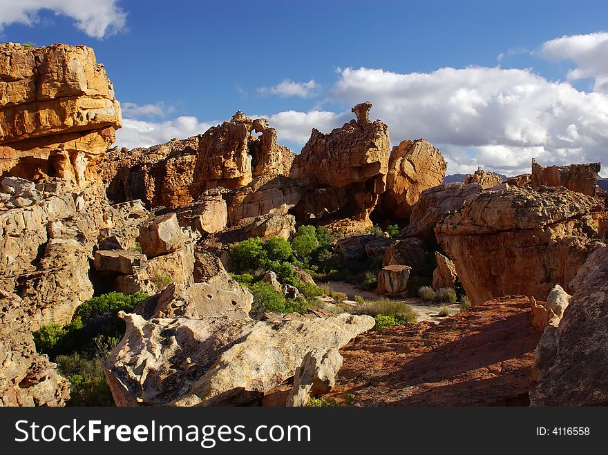 Yellow red stones and cliffs on red soil. Yellow sand and green bushes, deep blue cloudy sky. mountains of South Africa. Yellow red stones and cliffs on red soil. Yellow sand and green bushes, deep blue cloudy sky. mountains of South Africa