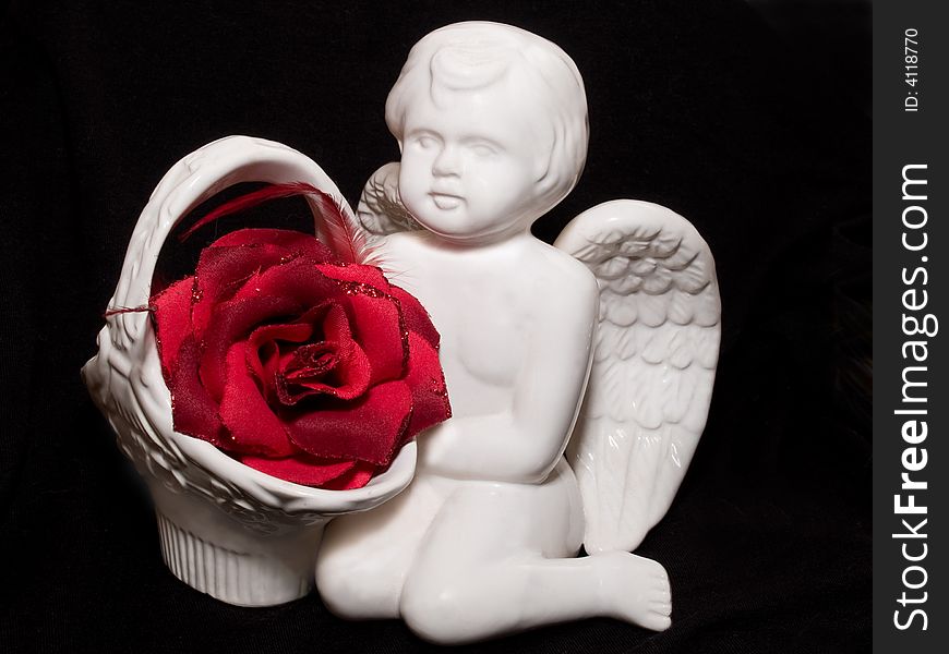 Still-life with valentine's gift with angel figure and red rose flower on black background