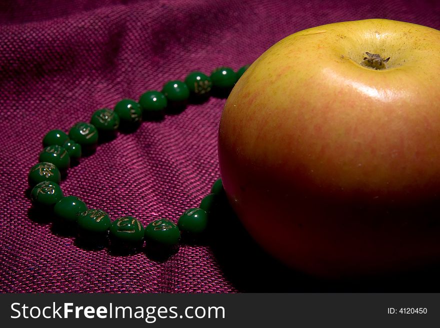 Single apple and necklace beads on the red background macro
