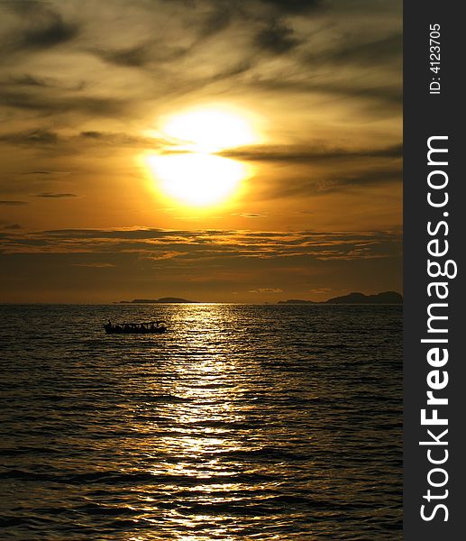 A setting sun by the sea with a boat cruising through its reflection. A setting sun by the sea with a boat cruising through its reflection