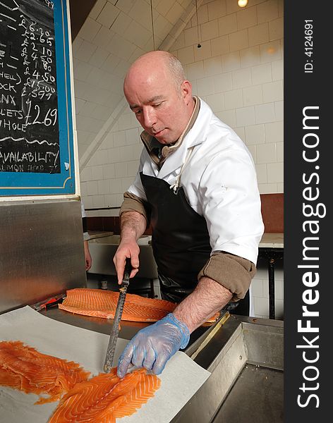 Fishmonger cutting slices of smoked salmon fresh from the smoke house. Fishmonger cutting slices of smoked salmon fresh from the smoke house