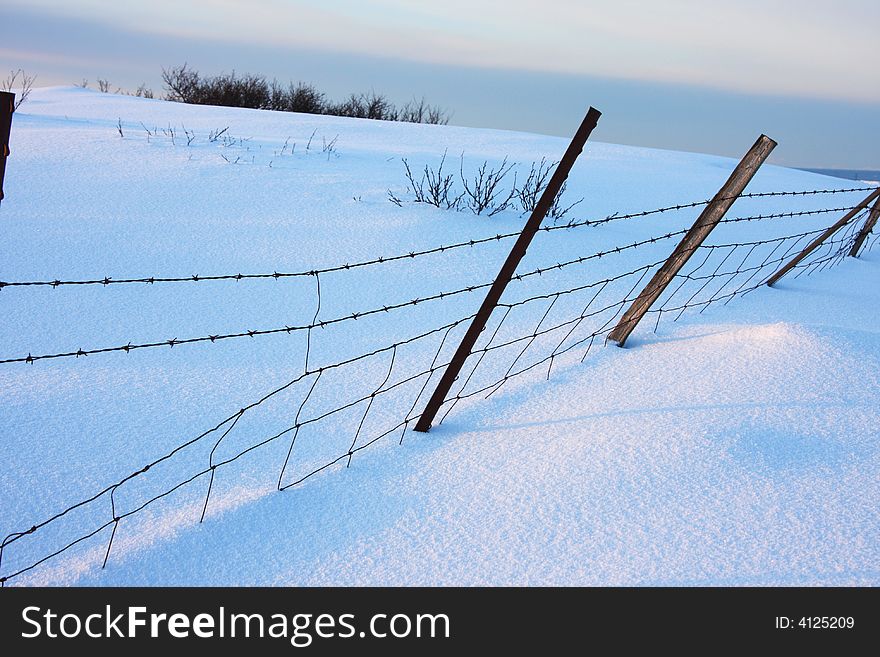 Barbed wire fence in winter, partly covered in snow. Barbed wire fence in winter, partly covered in snow