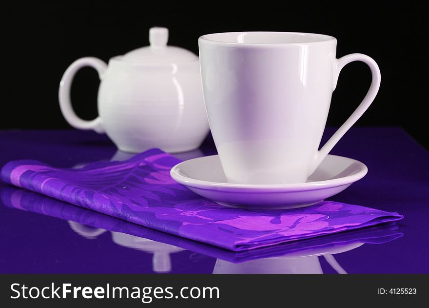 A coffee cup and teapot set on a blue/purple table table. A coffee cup and teapot set on a blue/purple table table