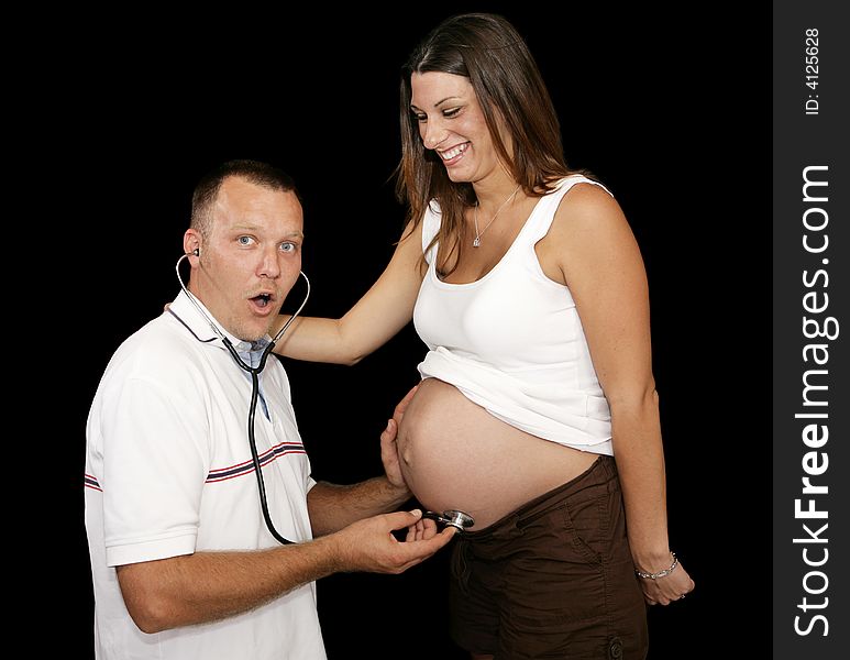 New father listening to his wife's pregnant belly with a stethescope.  Black background. New father listening to his wife's pregnant belly with a stethescope.  Black background