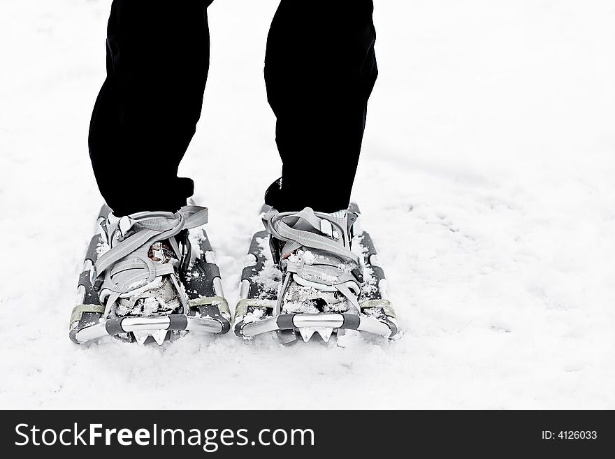 Someone wearing snowshoes in the snow.  Bottom half of legs down.