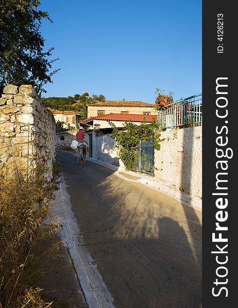 The image illustrates the quite and peaceful life of a typical village in southern Greece. A lone donkey rider is moving up the narrow path. The image illustrates the quite and peaceful life of a typical village in southern Greece. A lone donkey rider is moving up the narrow path.