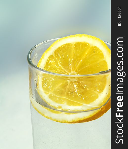 A fresh slice of lemon in a glass, on a blue background