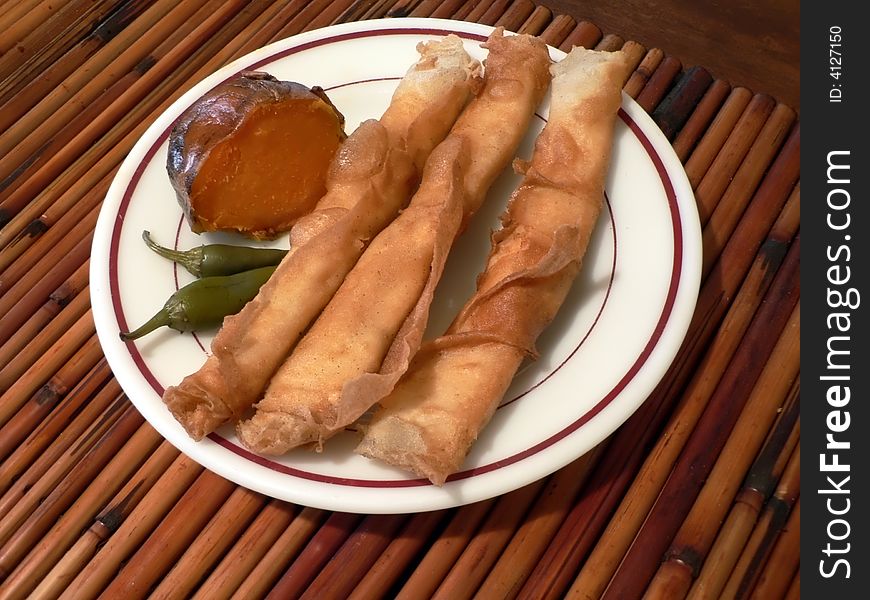 Three springrolls with sweet potato and hot pepers on a white dinner plate on top of a bamboo placemat. Three springrolls with sweet potato and hot pepers on a white dinner plate on top of a bamboo placemat