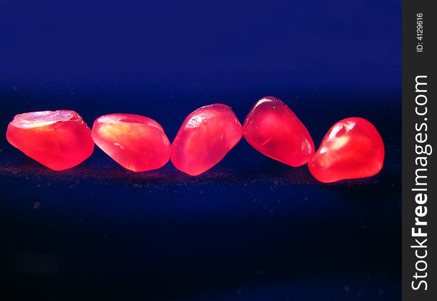 Five red grains of a pomegranate on a dark background