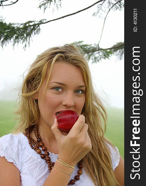 A pretty young blonde girl takes her first bite of a crisp red apple
