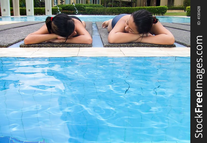 Two Asian girls suntanning at the edge of a quiet swimming pool. Two Asian girls suntanning at the edge of a quiet swimming pool