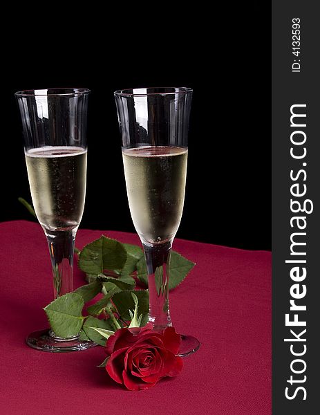 Two glassis of champagne with a single red rose on a red and black background. Two glassis of champagne with a single red rose on a red and black background