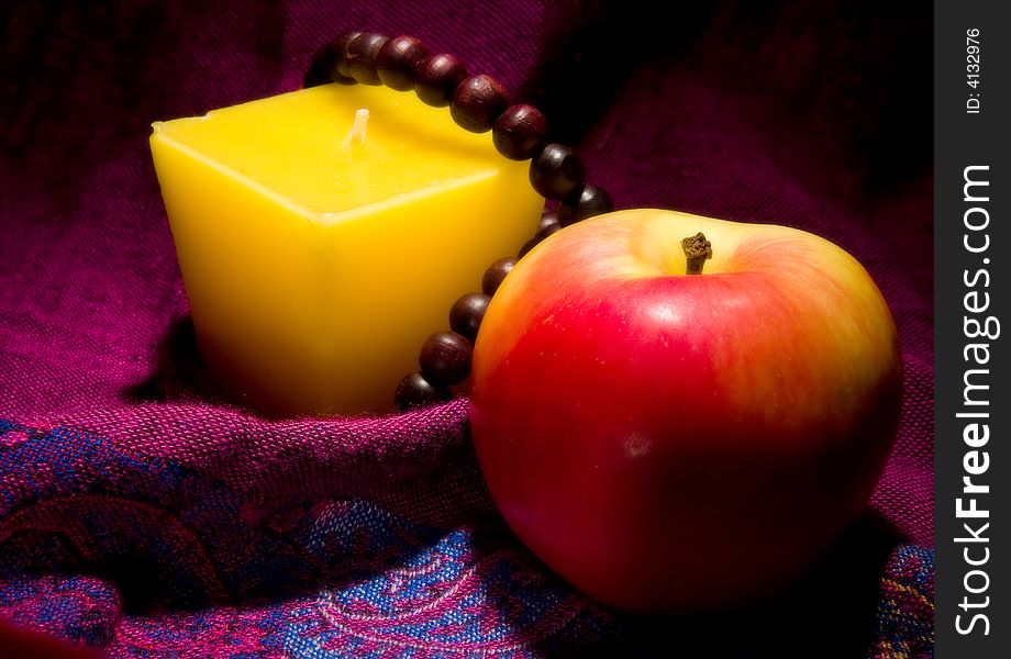 Candle and apple and wooden necklace on the red background macro. Candle and apple and wooden necklace on the red background macro