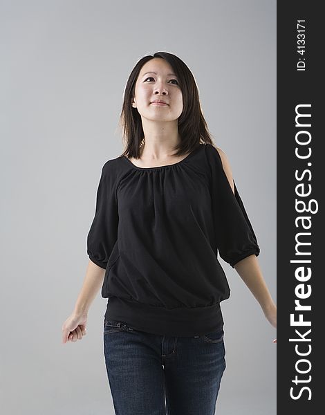 Young Asian woman wearing a black top and denim jeans walks forward with her head up against a gray studio background. Young Asian woman wearing a black top and denim jeans walks forward with her head up against a gray studio background.