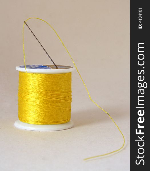 Yellow spool of thread with needle on a white background