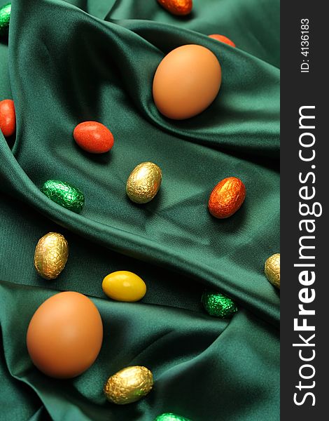 A selection of Easter eggs (natural and chocolate) lying on dark green satin fabric. A selection of Easter eggs (natural and chocolate) lying on dark green satin fabric.