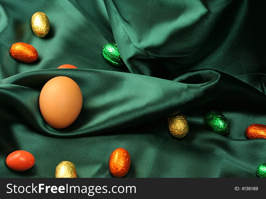 A selection of Easter eggs (natural and chocolate) lying on dark green satin fabric. A selection of Easter eggs (natural and chocolate) lying on dark green satin fabric.