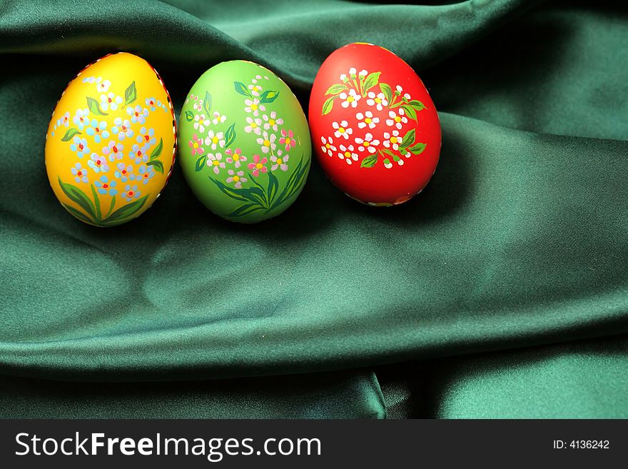 Three Easter eggs (red, yellow and green) lying on dark green satin fabric - textile. Three Easter eggs (red, yellow and green) lying on dark green satin fabric - textile.