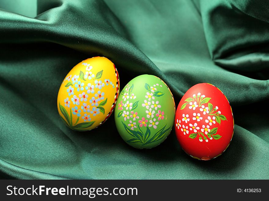 Three Easter eggs (red, yellow and green) lying on dark green satin fabric - textile. Three Easter eggs (red, yellow and green) lying on dark green satin fabric - textile.