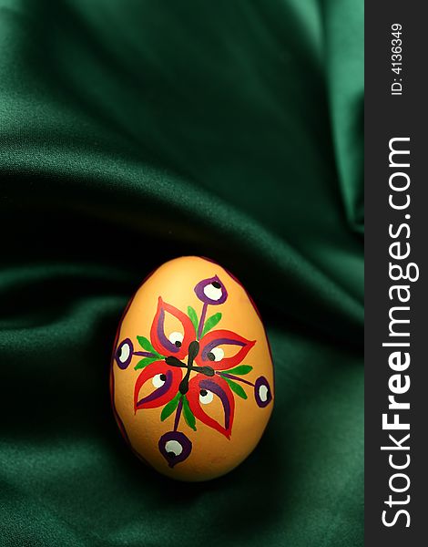 A detail of an Easter egg with colorful ornaments, lying on dark green satin fabric - background. A detail of an Easter egg with colorful ornaments, lying on dark green satin fabric - background.