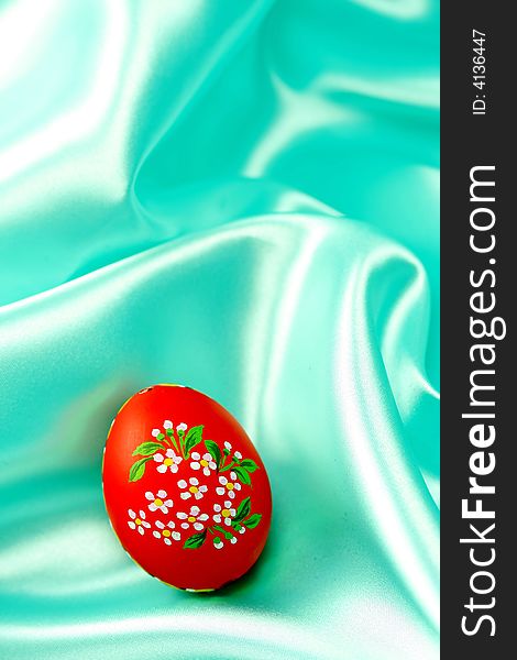A detail of a hand-painted Easter egg on turquoise satin fabric - background. A detail of a hand-painted Easter egg on turquoise satin fabric - background.