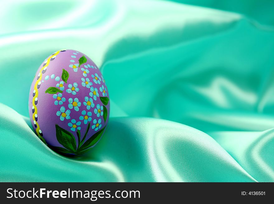 A detail of a hand-painted Easter egg on turquoise satin fabric - background. A detail of a hand-painted Easter egg on turquoise satin fabric - background.