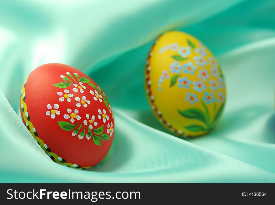 Two Easter eggs (red and yellow) lying on turquoise satin fabric - textile. Two Easter eggs (red and yellow) lying on turquoise satin fabric - textile.